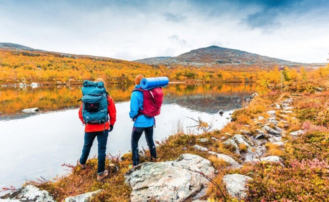 Två vandrare med ryggsäckar vid en fjällsjö i höstfärger
